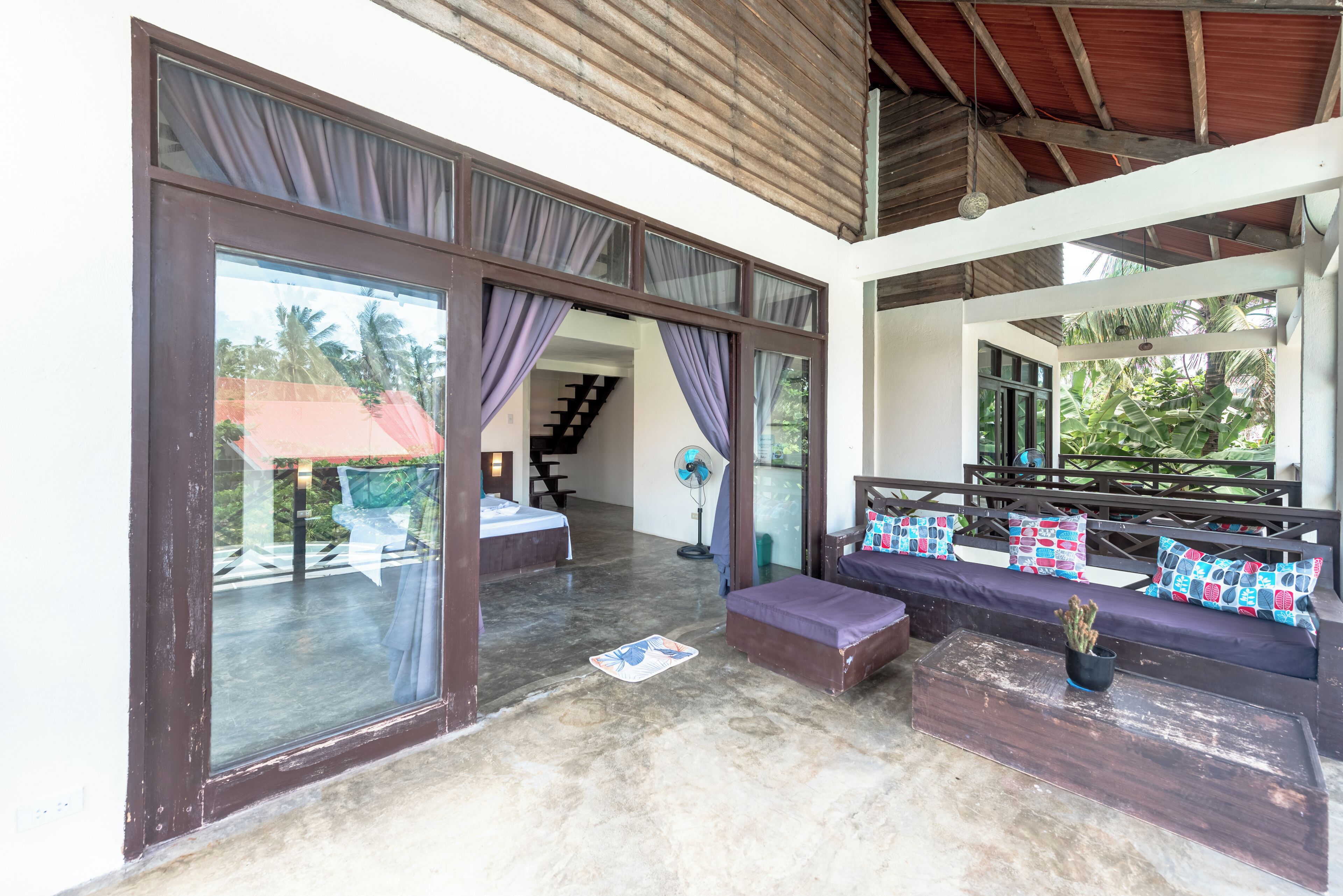 A spacious room with a large sliding glass door leading to a balcony, a sofa with patterned cushions, and a small table with a plant.