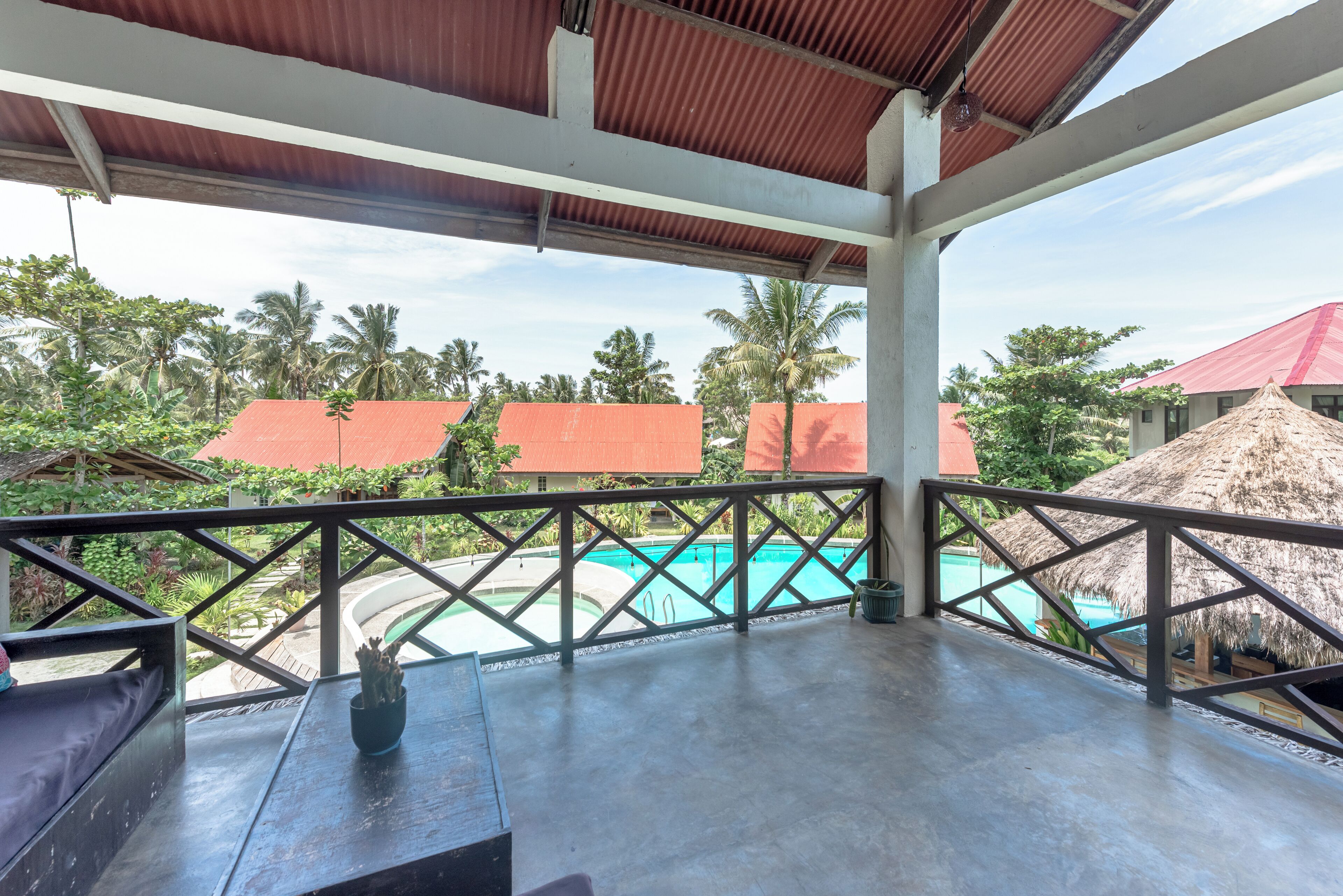 A covered outdoor area with a pool, wooden furniture, and a view of the surrounding buildings and palm trees.