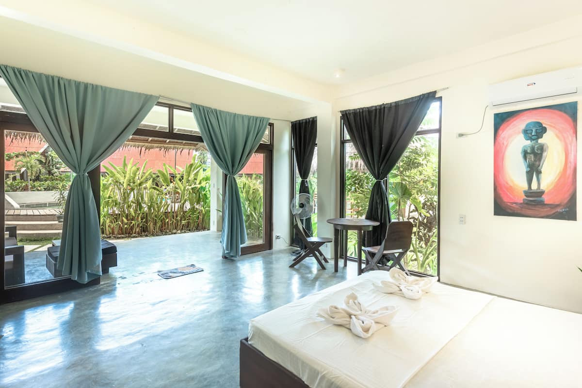 A hotel room with a bed, a small table, a chair, and a view of the outdoors.