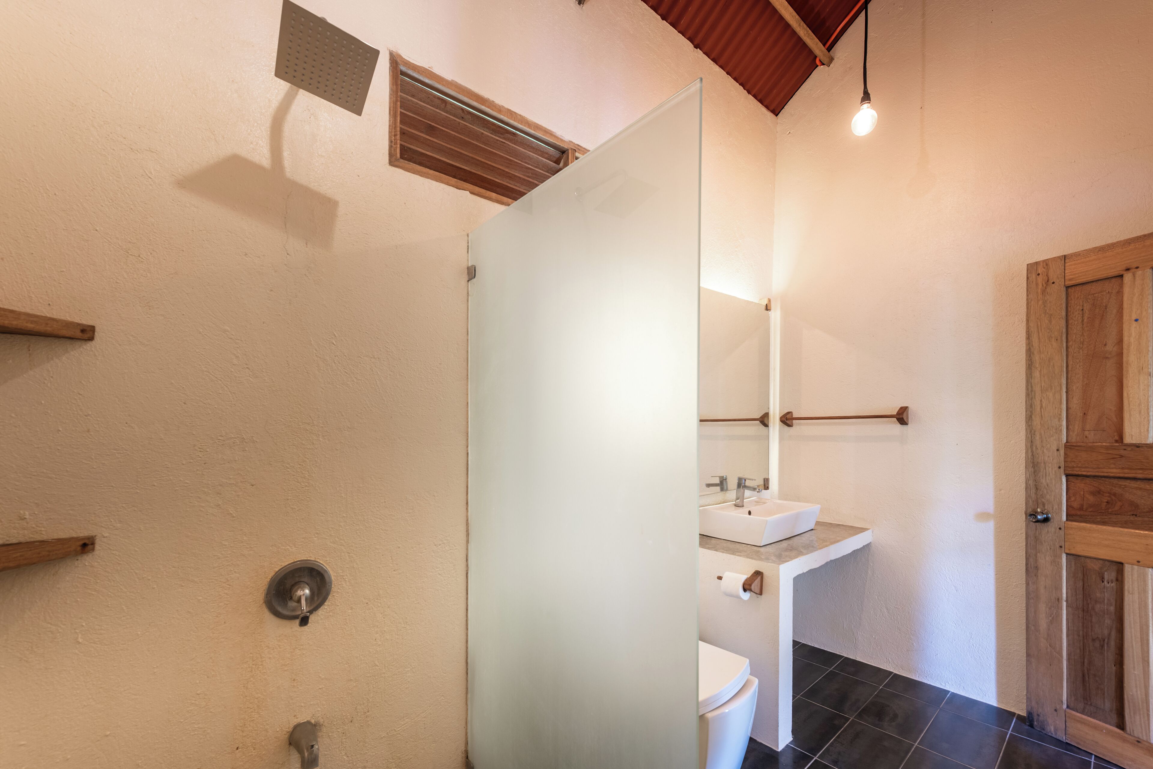 Un baño con mampara de vidrio, inodoro, lavamanos y puerta de madera.