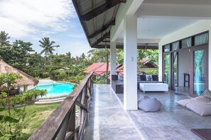A modern villa with a swimming pool, outdoor seating, and a view of the surrounding tropical landscape.