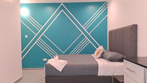 Une chambre à coucher moderne avec un motif géométrique sur le mur, un lit gris avec une couverture blanche et une tête de lit grise.