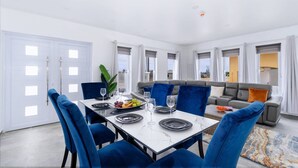 A modern dining area with a marble table, blue chairs, and a sofa with orange cushions.