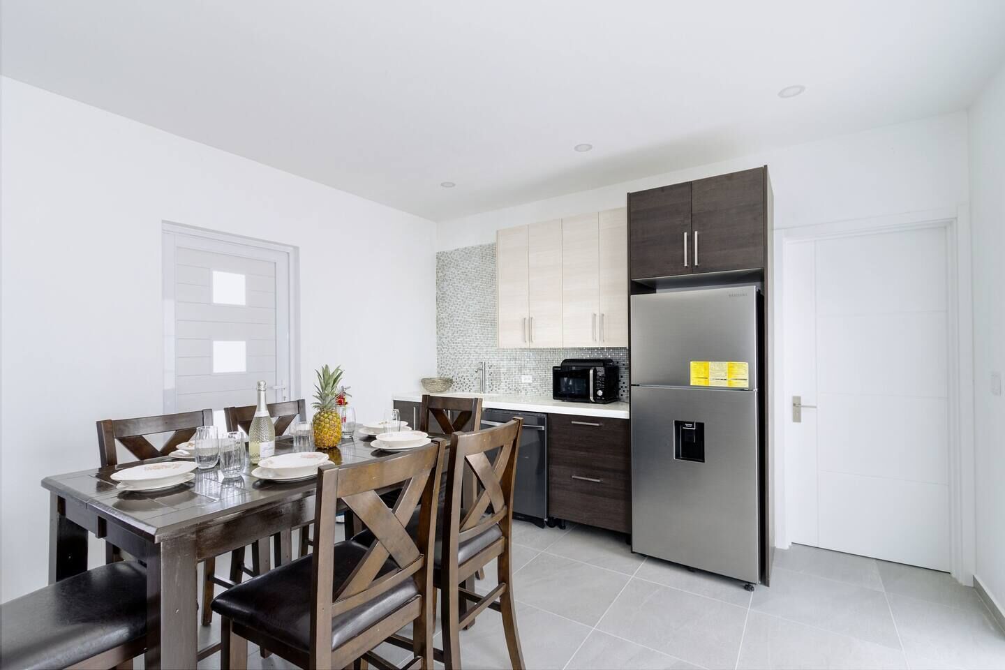 A modern kitchen with a dining table set for two, a refrigerator, and a microwave.