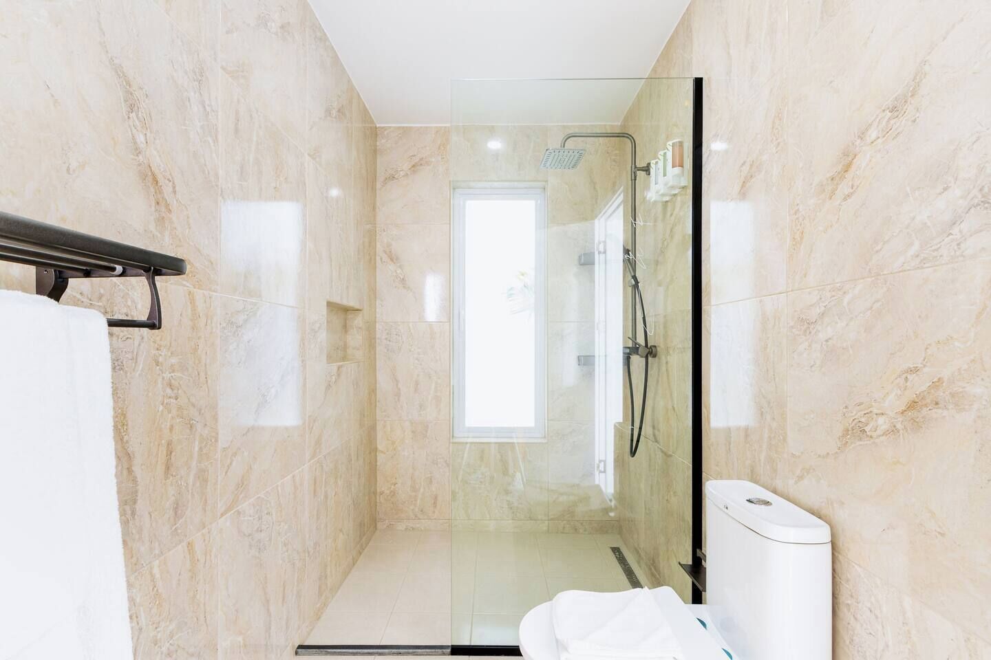 Ein modernes Badezimmer mit einer gläsernen Duschkabine, Marmorwänden und einer weißen Toilette.