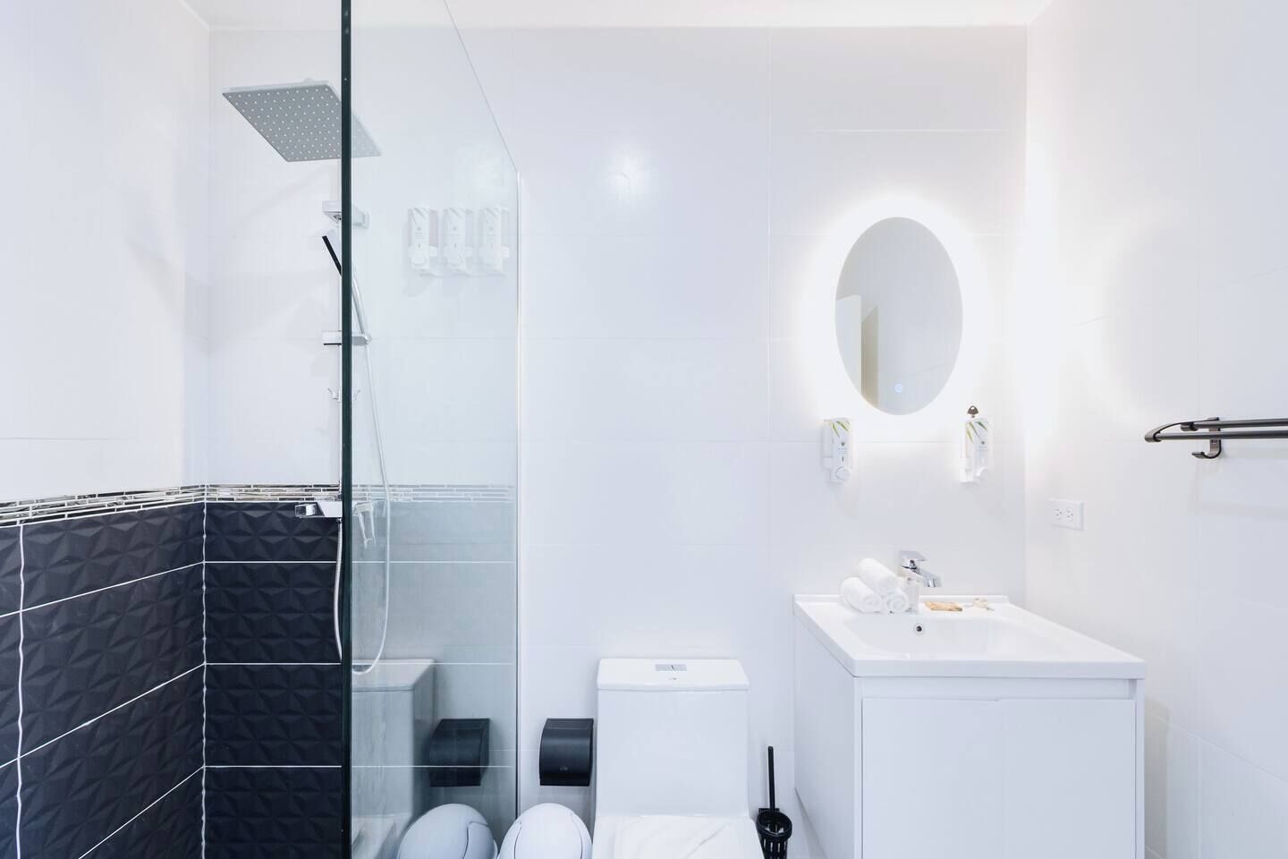 Un baño moderno con cabina de ducha de vidrio, un lavamanos blanco con espejo y un inodoro.