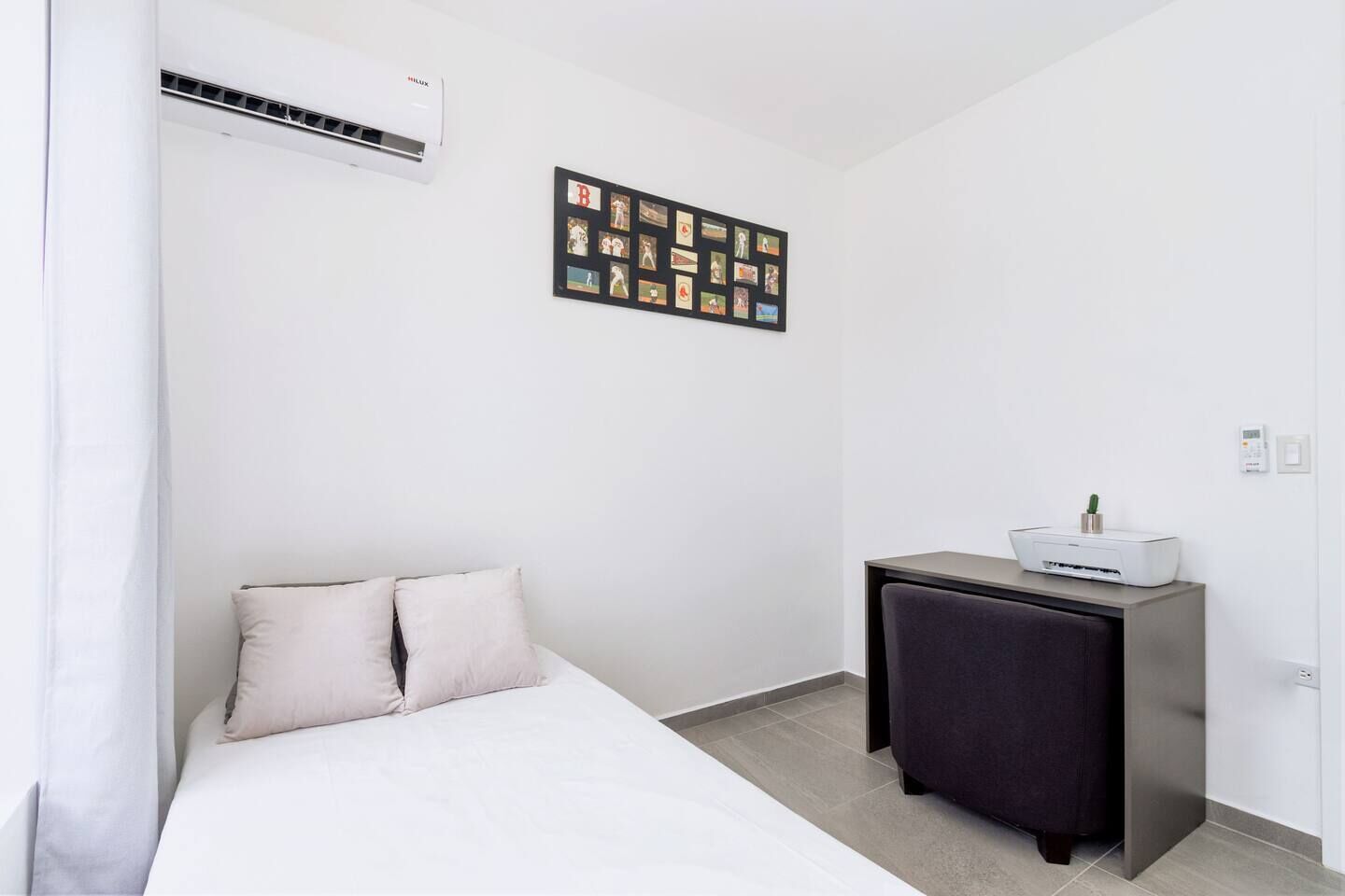 Hotellihuone, jossa on sänky, pieni työpöytä tulostimella ja seinälle kiinnitetty valokuvakollaasi.