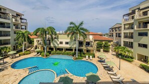 Een resort met een groot zwembad, omringd door ligbedden en palmbomen.
