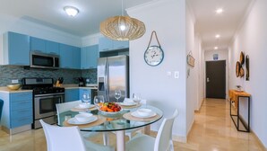 Een moderne keuken met blauwe kastjes, een roestvrijstalen koelkast en een glazen eettafel voor vier personen.