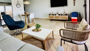 Een moderne woonkamer met een bank, fauteuil, salontafel en een aan de muur bevestigde televisie.