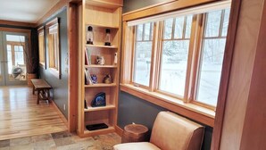 Una stanza accogliente con una libreria in legno, una poltrona in pelle e un'ampia finestra vista su un paesaggio innevato.