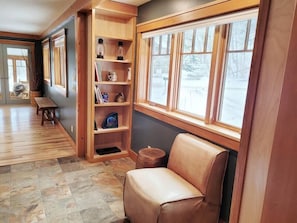 A cozy room with a wooden bookshelf, a leather chair, and a large window with a view of a snowy landscape.