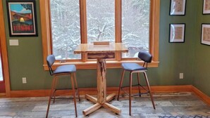 Zona pranzo con tavolo in legno e due sedie, ampia finestra vista alberi e opere d'arte appese alle pareti.