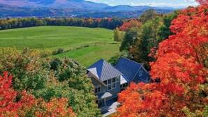 Ein Haus mit geneigtem Dach, umgeben von einem großen, grünen Feld und Herbstbäumen.