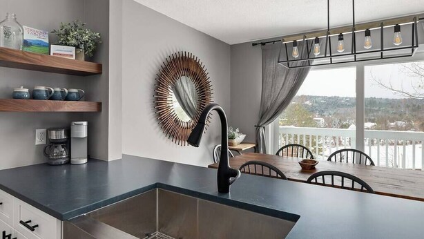 A modern kitchen with a black faucet, wooden shelves, a decorative mirror, and a dining area with a view.
