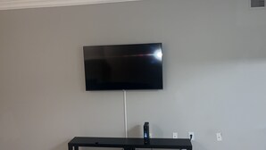 Una TV a schermo piatto montata su una parete spoglia, con un mobile basso nero sottostante.