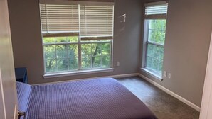 Una camera da letto con un letto, due finestre e vista sugli alberi.