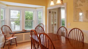 A dining room with a large wooden table and six chairs, large windows with a view of greenery, and a map on the wall. - Family Pet Friendly 4BR in N.E. Harbor[Millbrook] (Mount Desert)