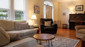 A living room with a sofa, armchair, and a small table. There is a piano and a lamp in the room. - Family Pet Friendly 4BR in N.E. Harbor[Millbrook] (Mount Desert)