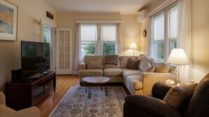 A living room with a sofa, a coffee table, a TV, and a lamp. - Family Pet Friendly 4BR in N.E. Harbor[Millbrook] (Mount Desert)