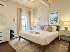 A bedroom with a large bed, bedside tables, a dresser, and a window with curtains. - Convenient 1 BR in Center of Acadia! [Willowbrook] (Mount Desert)