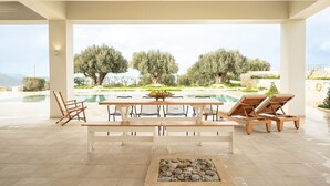 Un amplio espacio exterior para comer con vista a la piscina, muebles de madera y una chimenea de piedra.
