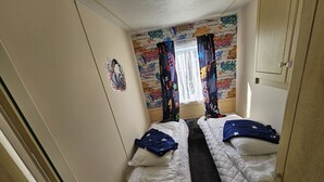 A small, narrow room with two beds, a window with colorful curtains, and a graffiti wall.