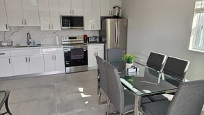 Une cuisine moderne avec des armoires blanches, un réfrigérateur en acier inoxydable, un four à micro-ondes et un four traditionnel. On y trouve une table à manger avec quatre chaises et une plante en pot posée sur la table.