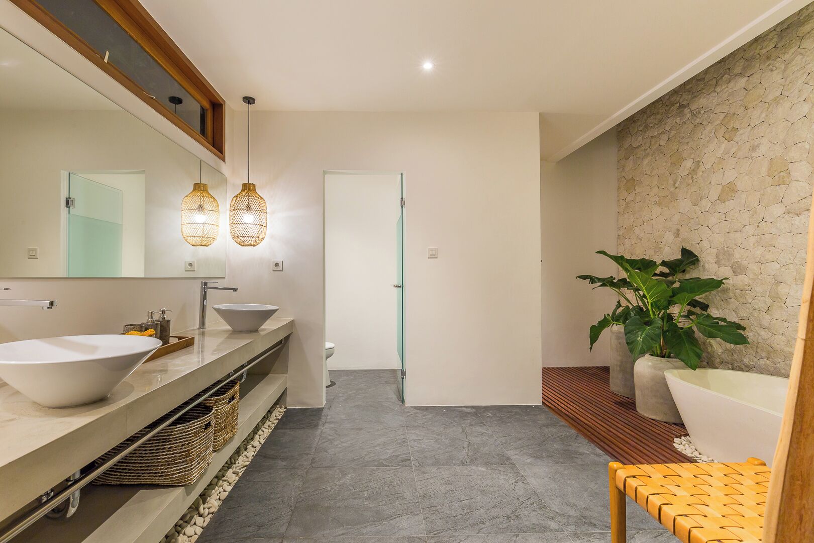 A modern bathroom with a large mirror, two sinks, a toilet, and a bathtub.