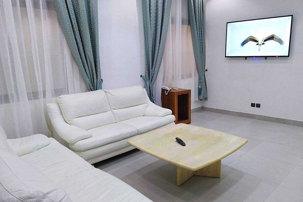 A living room with a white sofa, a wooden coffee table, and a TV on the wall.