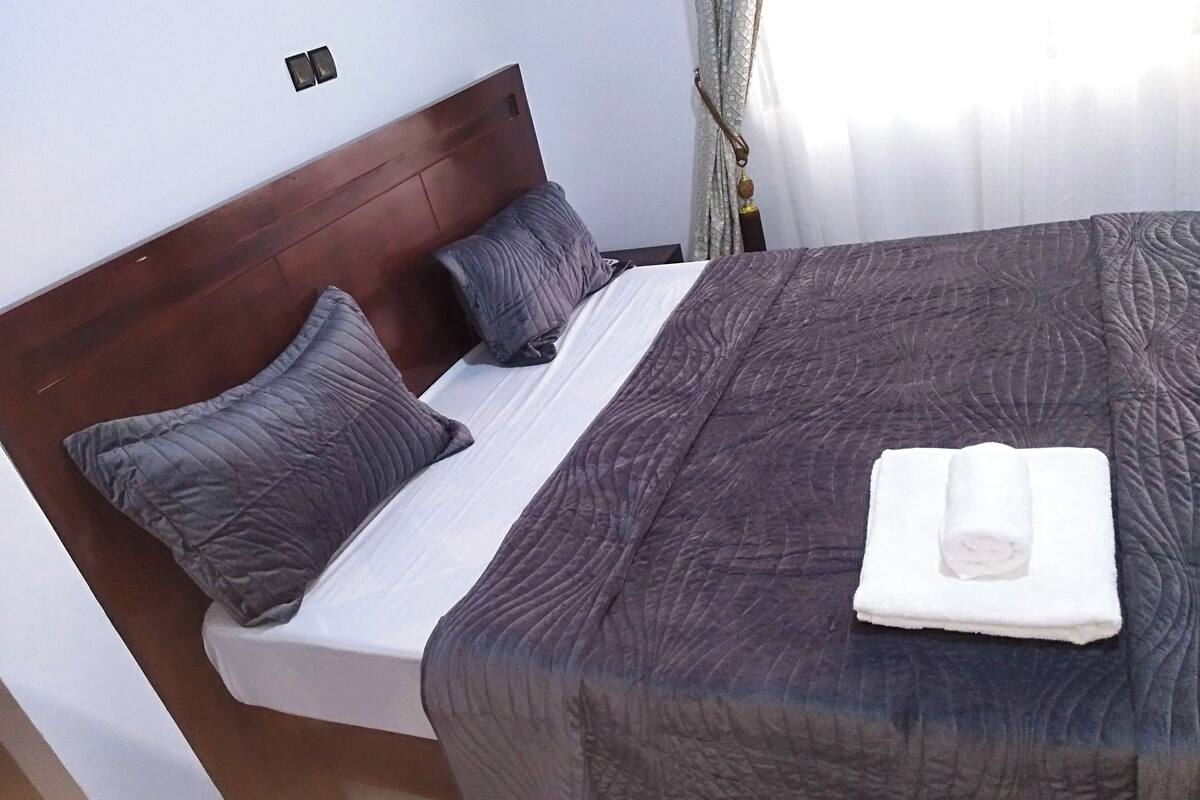 A neatly made bed with a dark quilt, two pillows, and a folded towel on the bed.