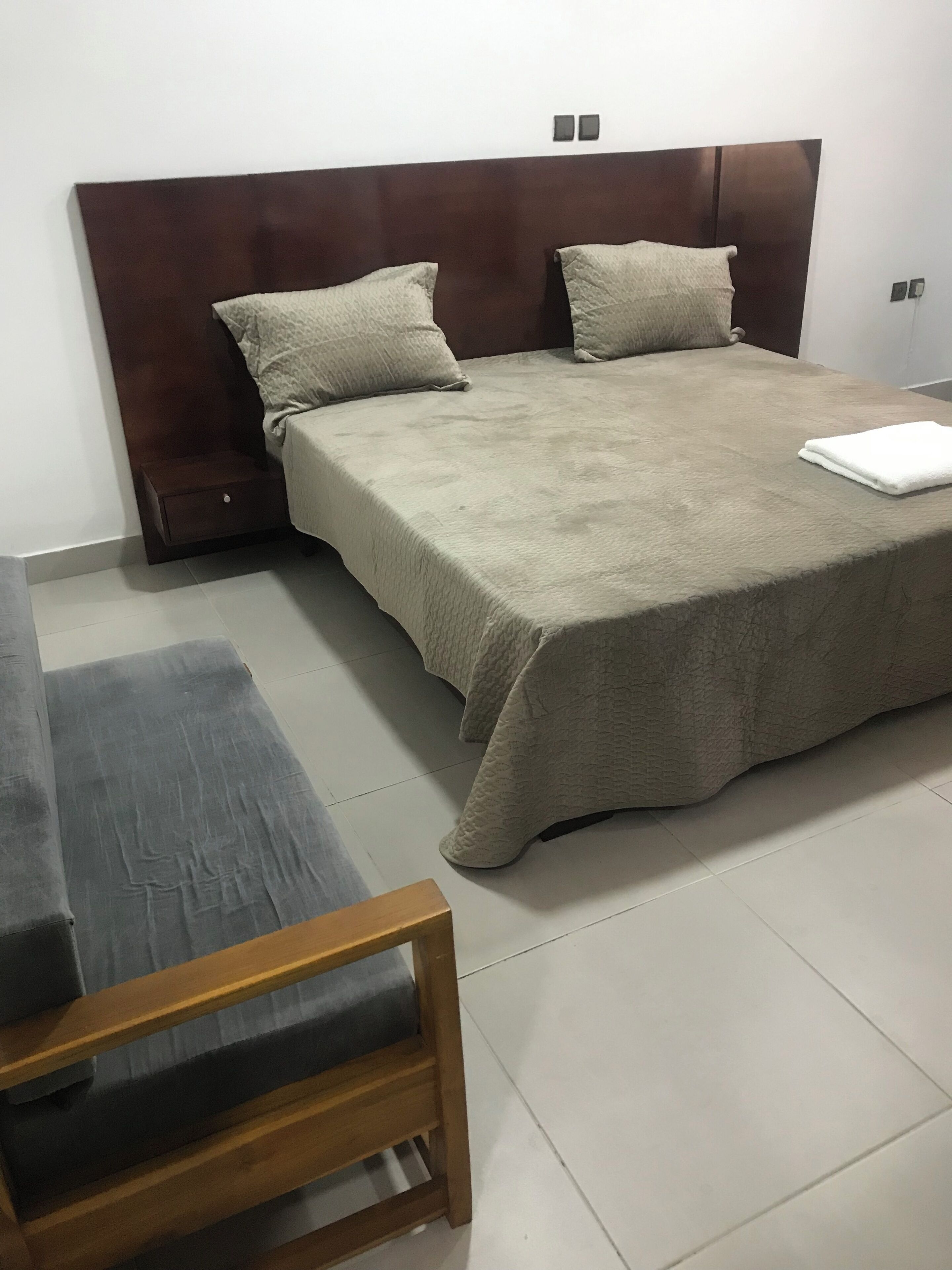Quarto bem arrumado com cama grande, duas almofadas, mesa de cabeceira e cadeira de madeira.