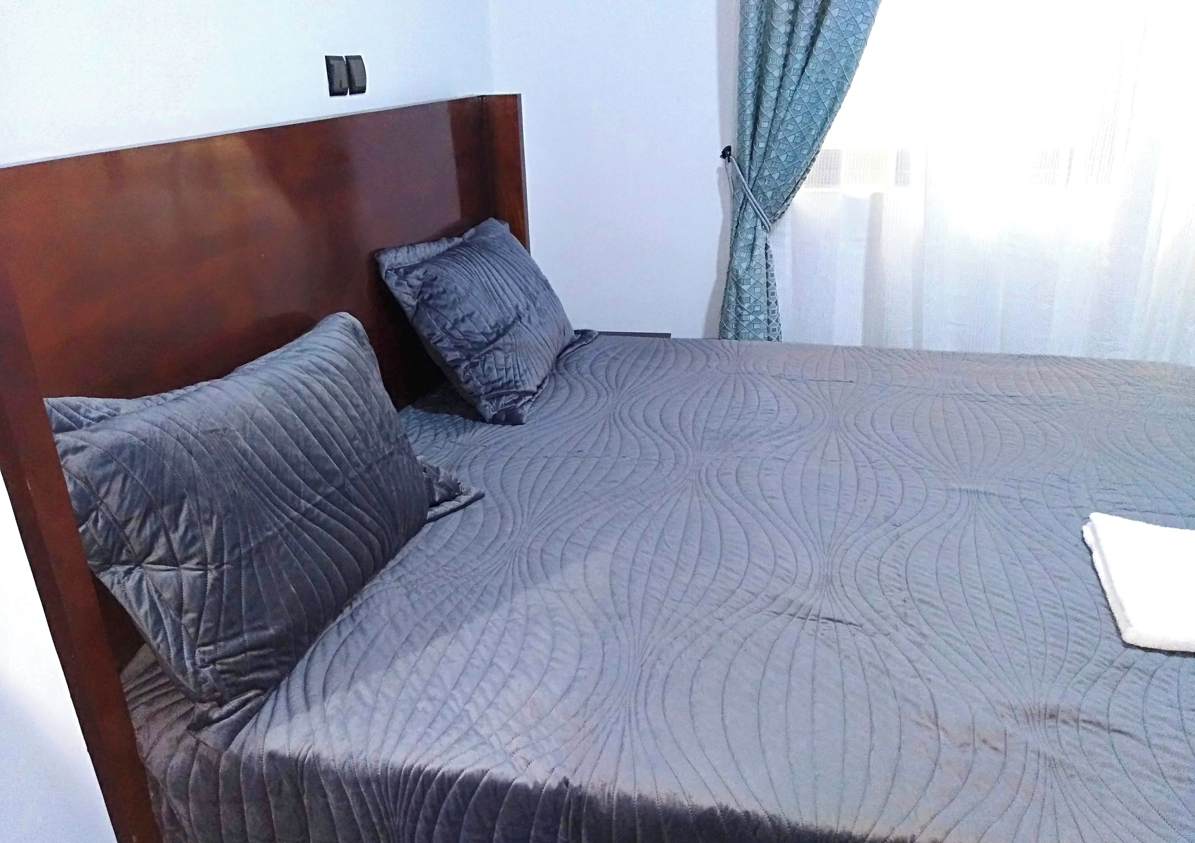 Uma cama bem arrumada com cabeceira de madeira e dois travesseiros.
