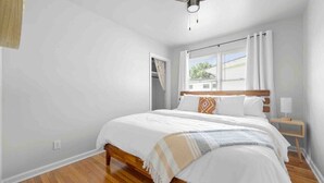 Ein Schlafzimmer mit einem hölzernen Bett, weißen Wänden, einem Fenster mit Vorhängen und einem Deckenventilator.