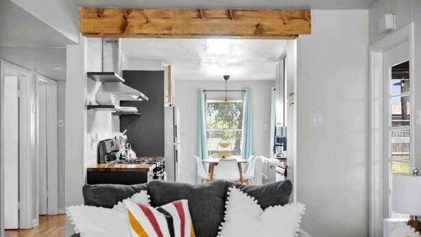 Ein modernes Wohnzimmer mit grauem Sofa, einem Holzbalken an der Decke und Blick in den Küchenbereich.