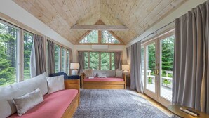 A room with a wooden ceiling, a bed with a pink mattress, a sofa, a nightstand with a lamp, and large windows with curtains. - Quiet Family & Pet Friendly Home! [Owls Nest] (Tremont)