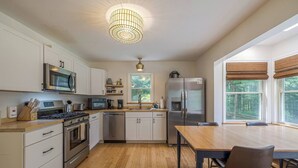 A modern kitchen with stainless steel appliances, wooden flooring, and large windows with views of trees. - Quiet Family & Pet Friendly Home! [Owls Nest] (Tremont)