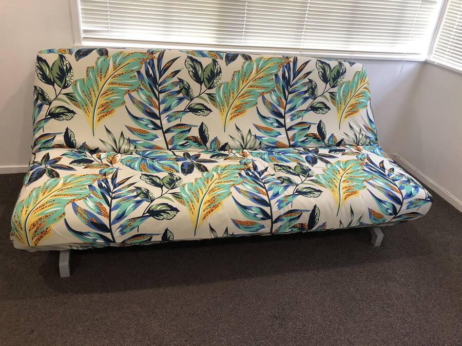 A sofa with a floral pattern, positioned in a room with a carpeted floor and a window with blinds.
