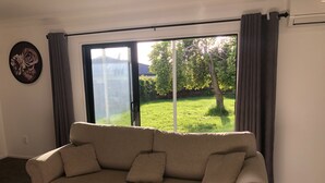 Un sofá color arena en una habitación con un amplio ventanal corredera que da a un área exterior con césped.