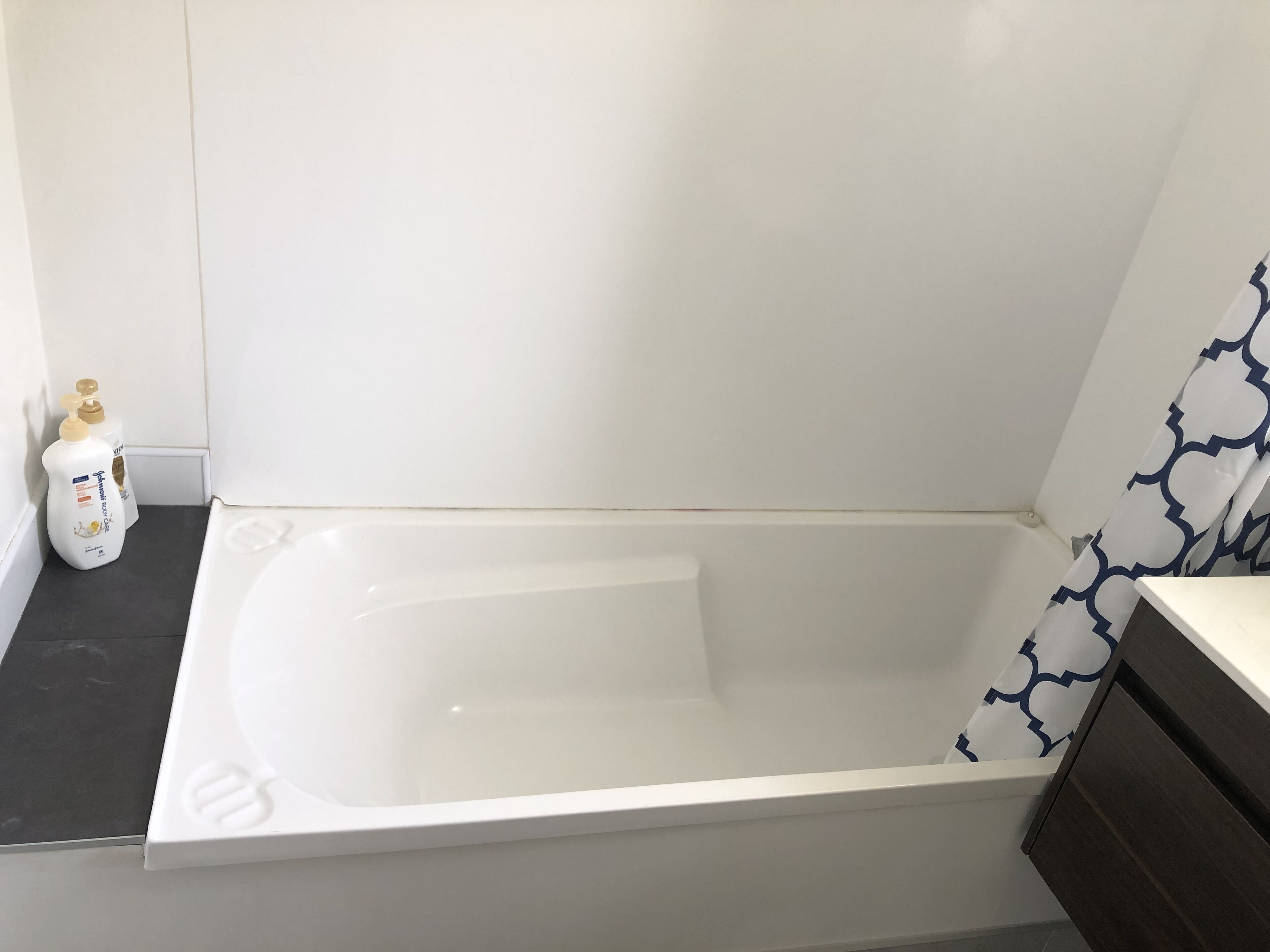 A modern bathroom with a white bathtub, a dark countertop, and a patterned shower curtain.
