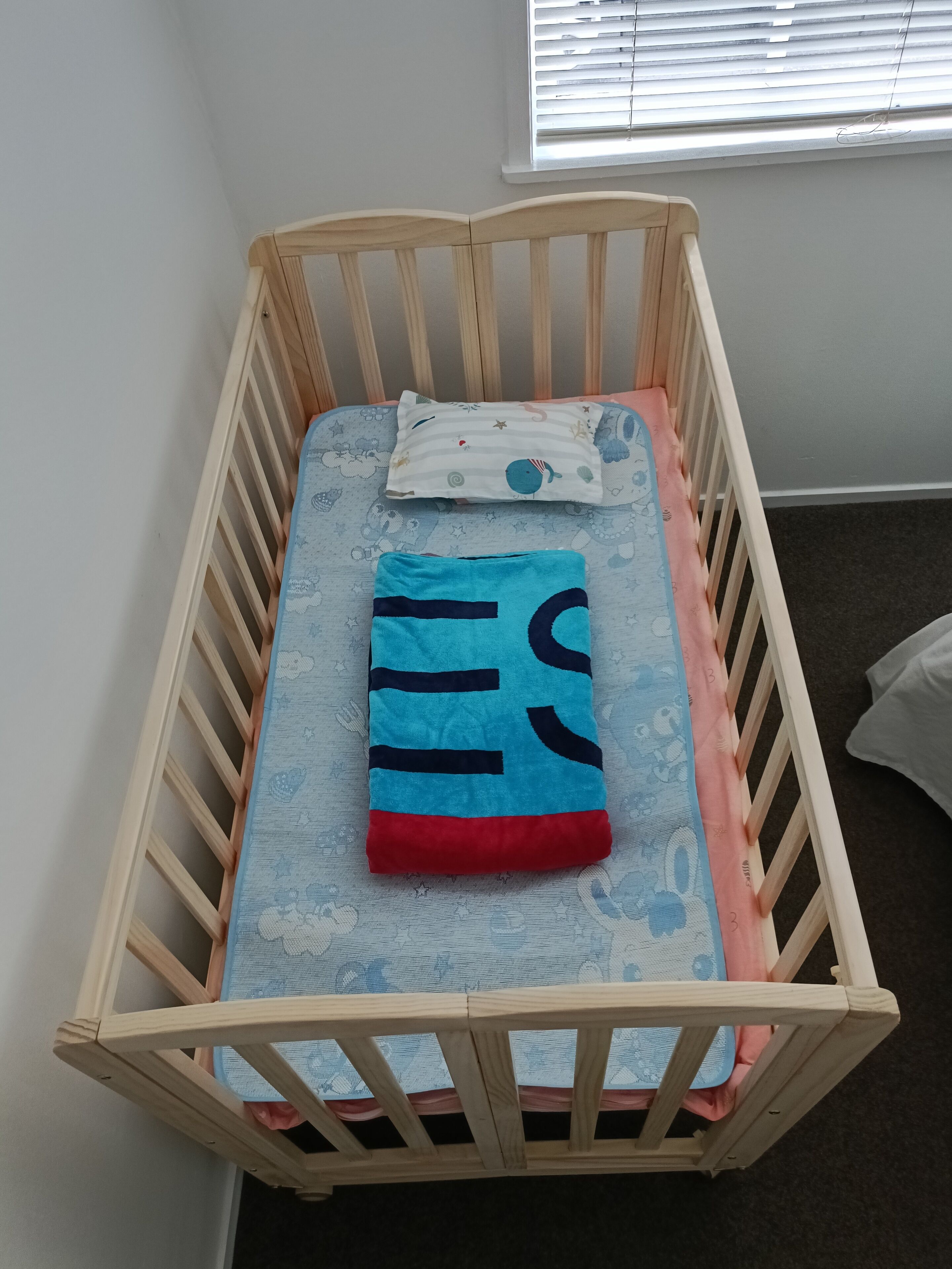 Een houten kinderbed met een blauwe matras en een rode deken.