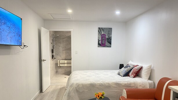 Un dormitorio moderno con una cama, una mesita con flores, un sofá de cuero rojo y un televisor en la pared.