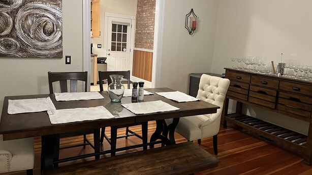 Un espace repas comprenant une table en bois, des chaises, un banc et un buffet avec des verres.