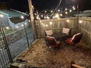 Une terrasse extérieure avec une clôture en bois, des guirlandes lumineuses et une table entourée de chaises.