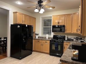 Une cuisine avec des meubles de rangement en bois, un réfrigérateur noir, une cuisinière, un four à micro-ondes et un ventilateur de plafond avec éclairage.