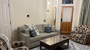 Un salon avec un canapé gris, des fauteuils à motifs, une table basse en bois et un tapis à motifs.