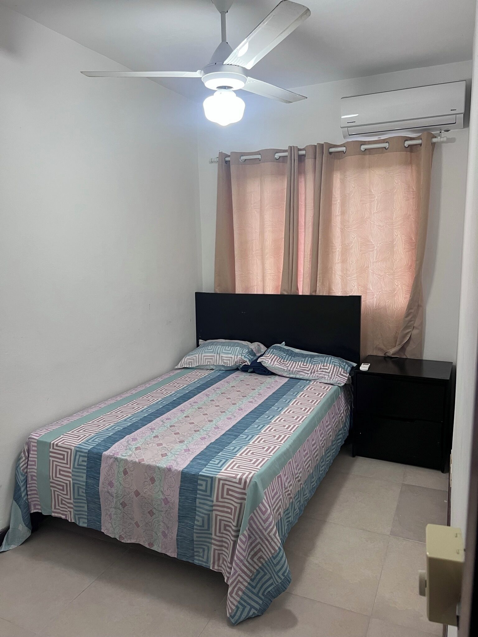 Une chambre à coucher comprenant un lit, une table de chevet, un ventilateur de plafond et un appareil de climatisation.