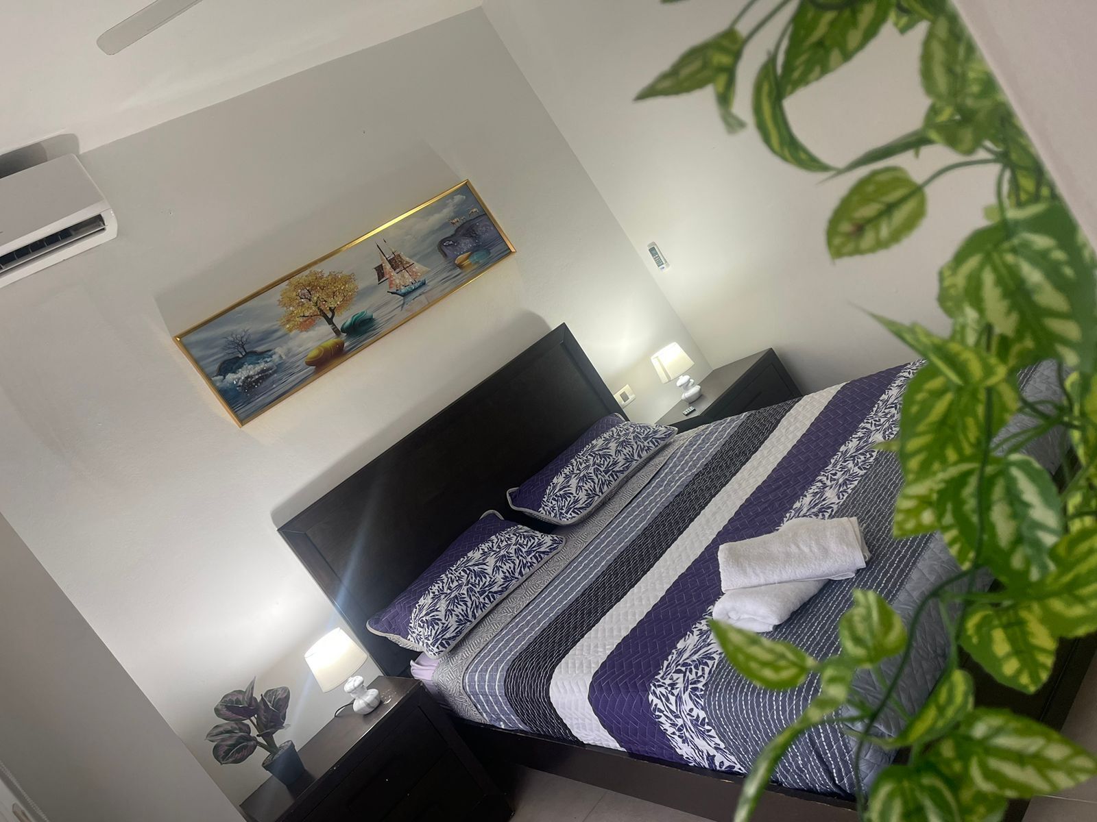 Une chambre d’hôtel moderne avec un grand lit, une table de chevet, une petite table de nuit avec une lampe et un climatiseur fixé au mur.