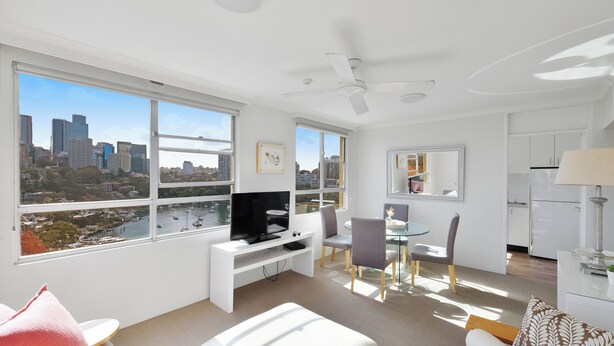 Una sala moderna con vista a la ciudad, televisor de pantalla plana, comedor y cocina.