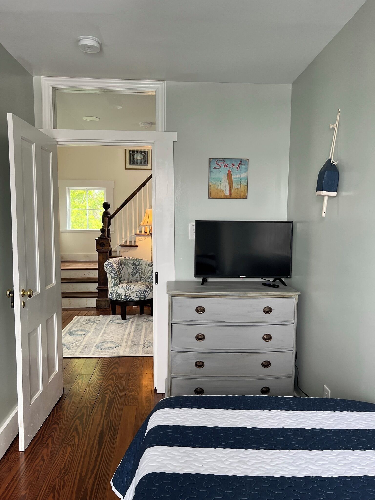 A bedroom with a bed, a dresser, a television, and a painting on the wall.